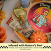 Two Blazy Susan tea leaf cone snack packs are arranged on a round wooden tray with a decorative vintage-style Blazy sign, autumn leaves, a small pumpkin, and a candle. Text at the bottom reads 'Infused with Nature's Best' and 'Premium, plant based ingredients for a cleaner smoke and richer flavor.
