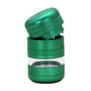 A green metal herb grinder with a transparent glass chamber in the middle, shown with the top lid removed and tilted, on a plain white background.