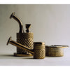A set of three vintage brass smoking accessories, including a water pipe, a small container, and a lid, all featuring a textured diamond-patterned finish, set against a neutral gray background.