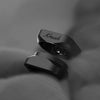 Two matte black metal rings with a polished finish, one featuring the script engraving 'Krush', displayed on a soft gray fabric background.