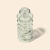 A clear glass bong with a ribbed cylindrical body and a small rounded top, photographed on a warm beige background with a soft shadow to the right.