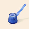 A translucent blue glass smoking pipe by NWTN Home with a flared ribbed base and a long angled stem, photographed on a plain warm beige background.