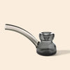 A small smoked glass water pipe with a curved stem and a double-bulb bowl, made of translucent dark gray glass, set against a solid light beige background.