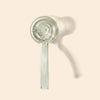 A clear glass hand pipe with a long, straight handle and a circular bowl, shown against a solid pale beige background with a soft shadow.