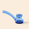 A translucent blue glass water pipe by NWTN Home with a curved bowl and a short neck, shown on a solid light beige background.